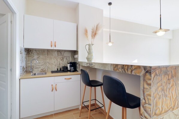 A modern kitchen with white cabinets, a marble backsplash, and two black bar stools. - Monastiraki 507 Superhost Hub (Athens)