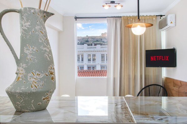 A modern room with a marble table, a unique vase, a view of buildings, a Netflix sign, and a hanging light fixture. - Monastiraki 507 Superhost Hub (Athens)