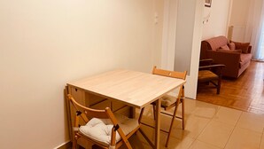 Ein Essbereich mit Holztisch und -stühlen, einer Couch im Hintergrund und einem Fliesenboden.