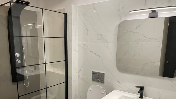 Un baño moderno con ducha envuelta en vidrio, inodoro, lavamanos y espejo.