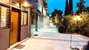 Vista nocturna de una calle con edificios, aceras y algo de vegetación.