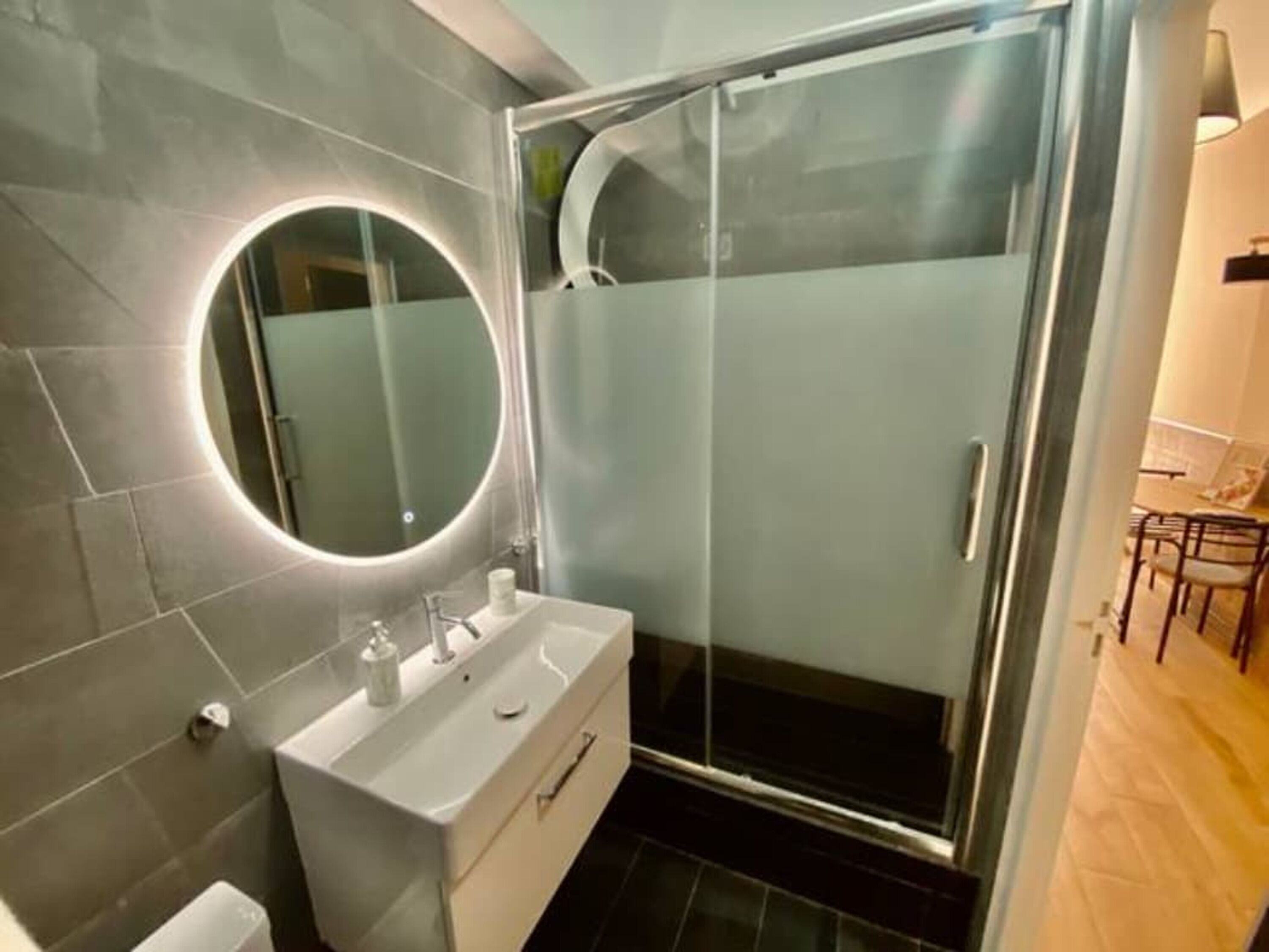 A modern bathroom with a glass-enclosed shower, a round mirror, and a white vanity.