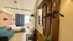Une chambre d’hôtel moderne comprenant un lit, une petite table, une chaise, un canapé bleu, une plante et un mur en bois muni de crochets.