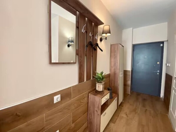 A hallway with a wooden floor, a mirror, wall-mounted lights, a potted plant, and a door. - Monastiraki 306 Superhost Hub (Athens)