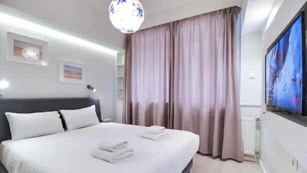 A modern hotel room with a large bed, a flat-screen TV on the wall, and a large window with curtains. - Monastiraki 107 Superhost Hub (Athens)