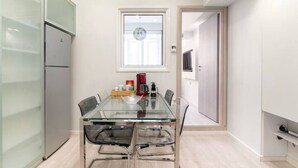 A modern kitchen with a glass dining table, a refrigerator, and a window above the sink. - Monastiraki 107 Superhost Hub (Athens)