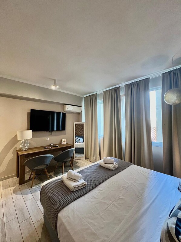 A hotel room with a large bed, a desk with a chair, a television, and a window with curtains.
