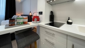 Una cocina moderna con encimera blanca, un hervidor rojo, una placa de inducción negra y una pequeña botella negra sobre la encimera.