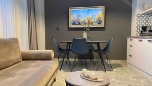 A modern living room with a beige sofa, a dining table with chairs, a coffee machine, and a painting on the wall. - Monastiraki 112 - 38m2 Superhost Hub (Athens)