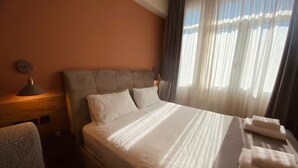 A hotel room with a large bed, a headboard, a nightstand, and a window with sheer curtains.