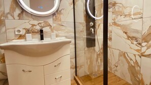 A bathroom with a white vanity, a round mirror with a light, and a glass shower enclosure.