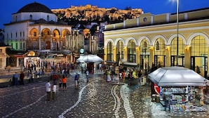 A cobblestone square with historic buildings, a prominent dome, and a view of a hill with a fortification.