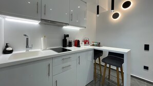 A modern kitchen with white cabinets, a black countertop, and a built-in stove. There are two bar stools and a small island with a sink. - Monastiraki 512 Superhost Hub (Athens)