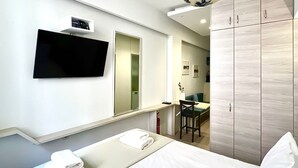 Habitación de hotel con cama, televisor en la pared, armario y escritorio con silla.