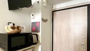 Una kitchenette compacta con microondas, hervidor y un cuenco de madera pequeño sobre la encimera.