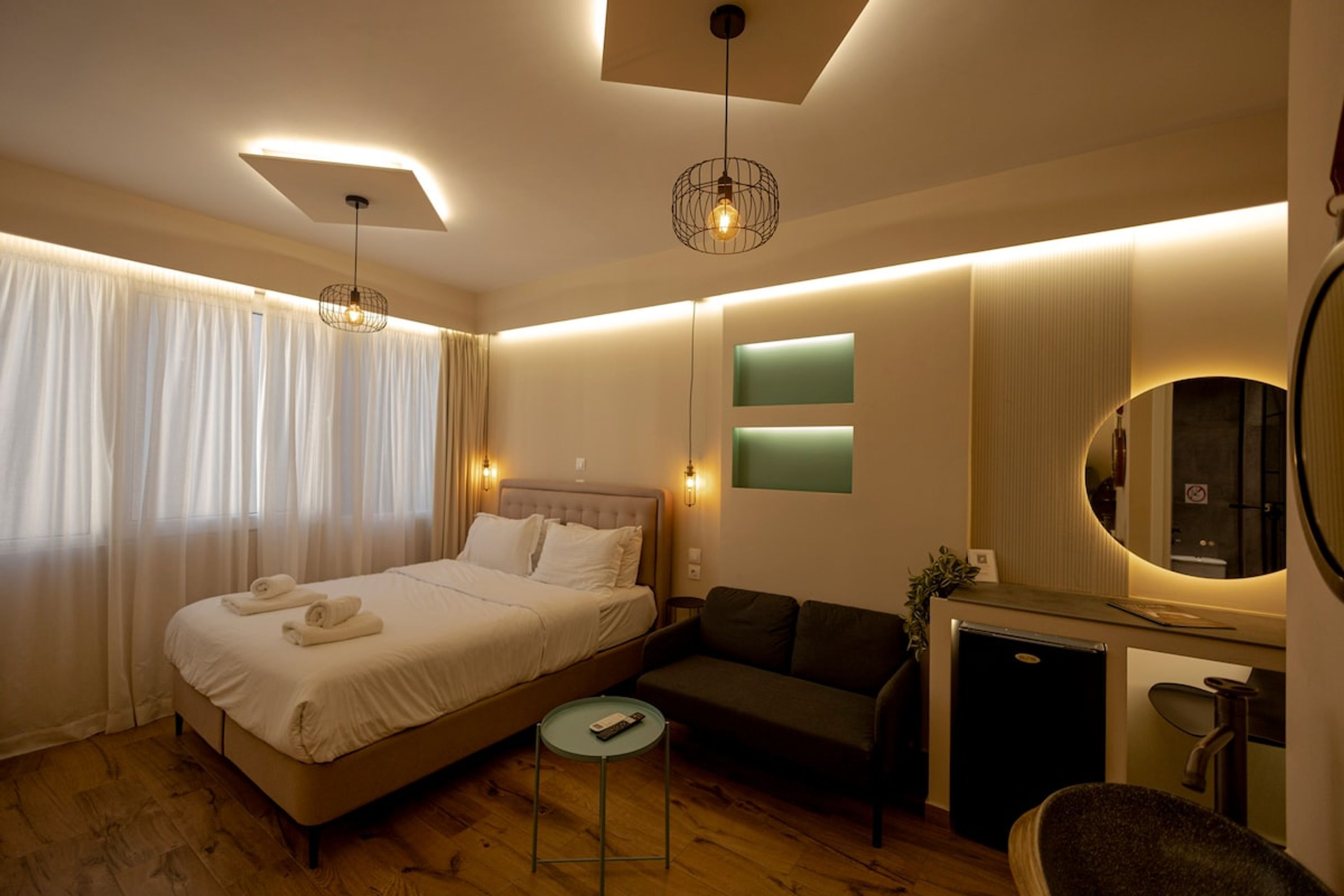 A modern hotel room with a bed, a sofa, a small table, a desk, and a mirror.