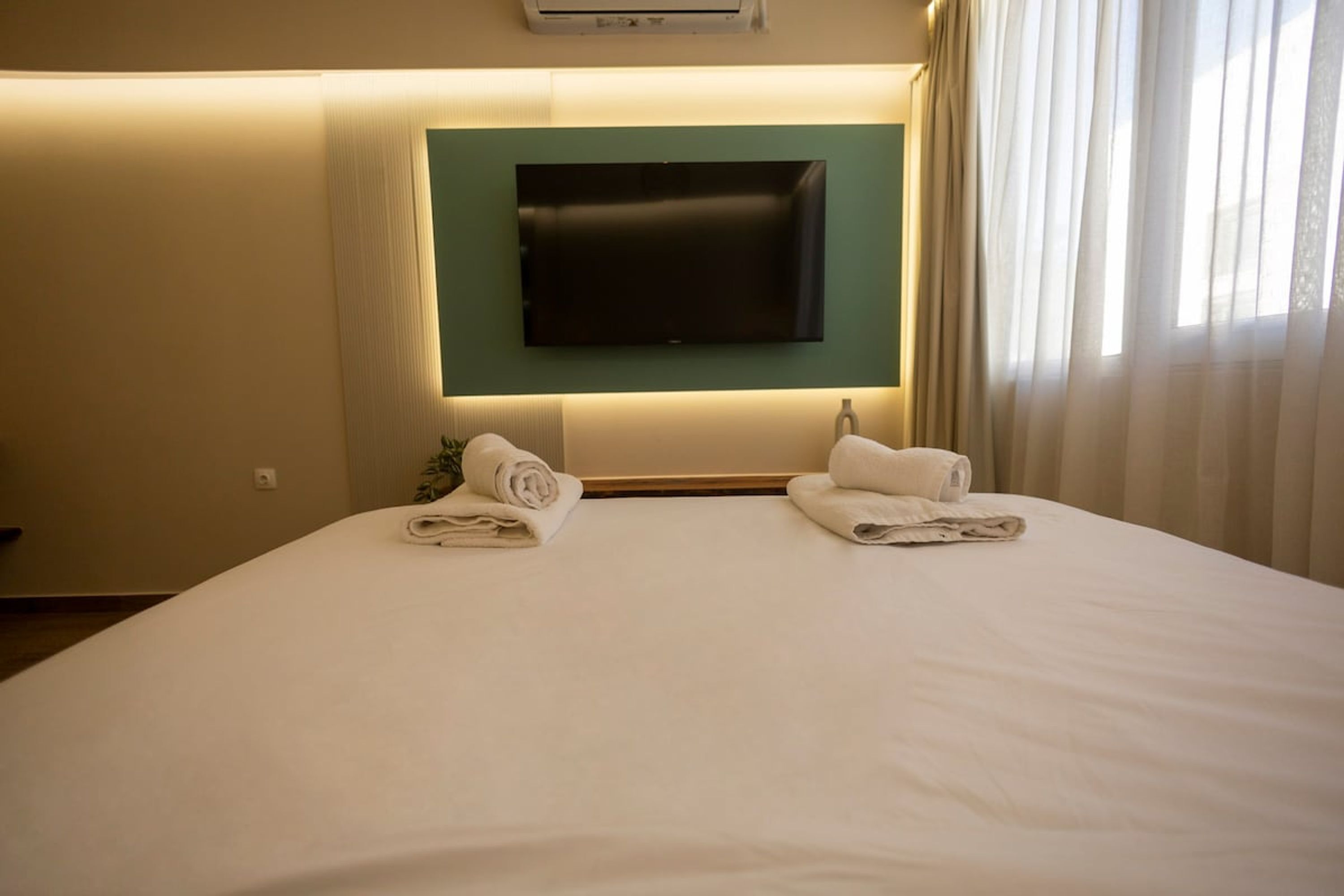 Une chambre d’hôtel avec un grand lit, un téléviseur à écran plat fixé au mur et deux serviettes enroulées posées sur le lit.