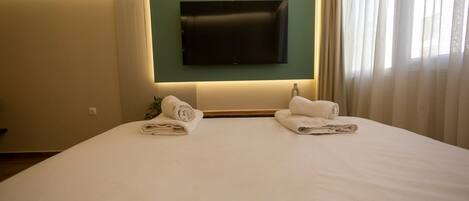 Habitación de hotel con una cama grande, un televisor de pantalla plana en la pared y dos toallas enrolladas sobre la cama.