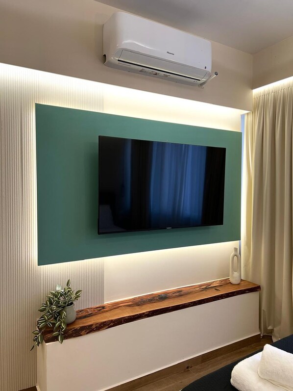 Een moderne hotelkamer met een wandgemonteerde flatscreen-tv, een houten console tafel, een potplant en een witte airconditioning.