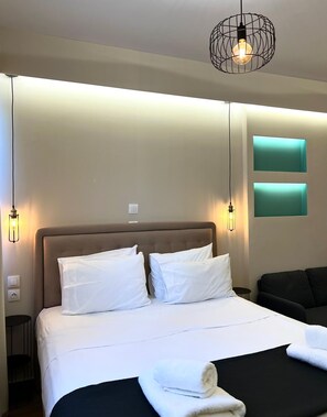 A hotel room with a large bed, two bedside lamps, a headboard, a black sofa, and two wall-mounted light panels. - Monastiraki 308 Superhost Hub (Athens)