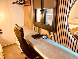 A compact, modern room with a wooden slat wall, a small window, a desk with a chair, and a bed with a white headboard.