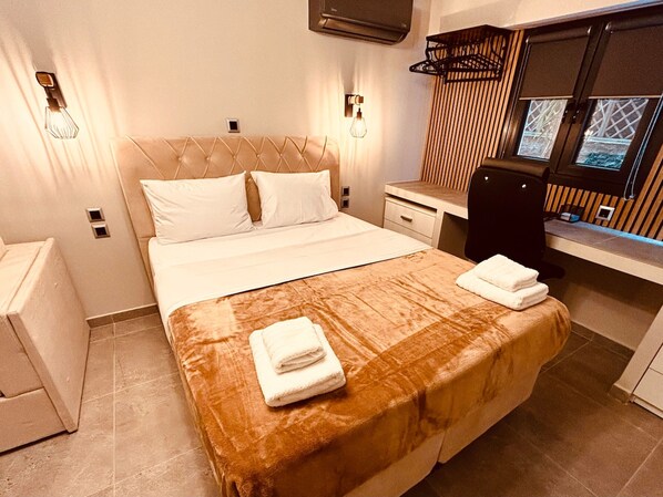 A modern hotel room with a large bed, bedside tables, a desk, and a window with blinds.