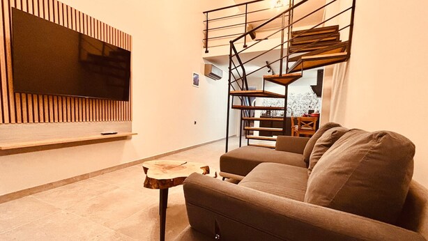 Een moderne woonkamer met een grote flatscreen televisie aan de muur, een houten salontafel, een bank en een wenteltrap.