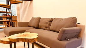 Een moderne woonkamer met een bruine modulaire bank, een houten salontafel en een wit gordijn op de achtergrond.