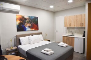 A hotel room with a bed, a painting, a desk, a chair, a sink, and a small kitchenette. - Athens Zeus A by Super Host Hub (Athens)