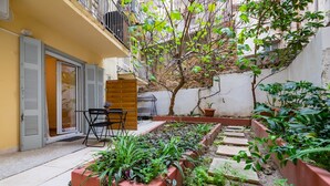 Un patio con un banco de madera, plantas en macetas y un pequeño árbol.