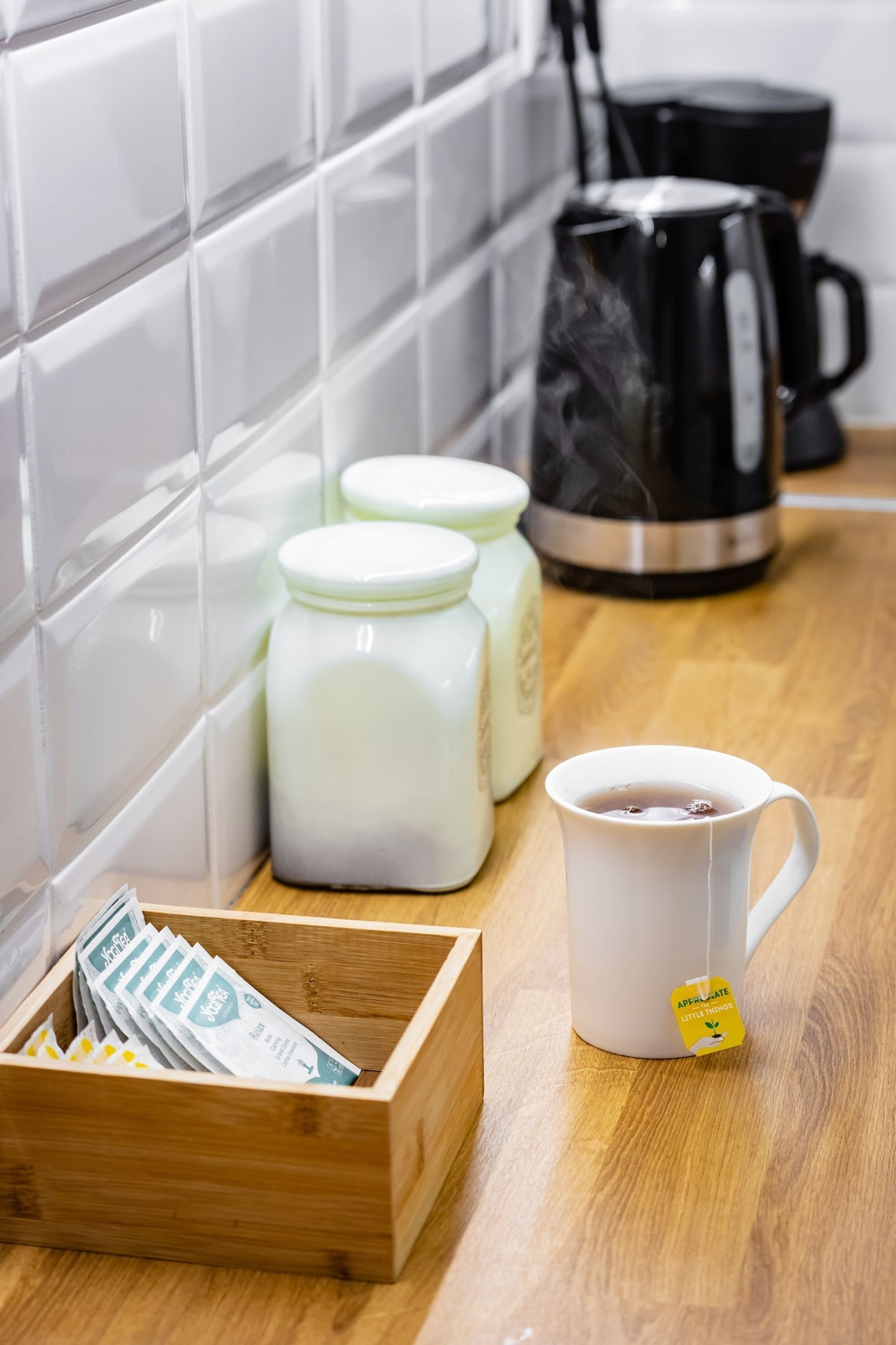 A kitchen counter with a coffee maker, jars, a wooden box, and a mug.