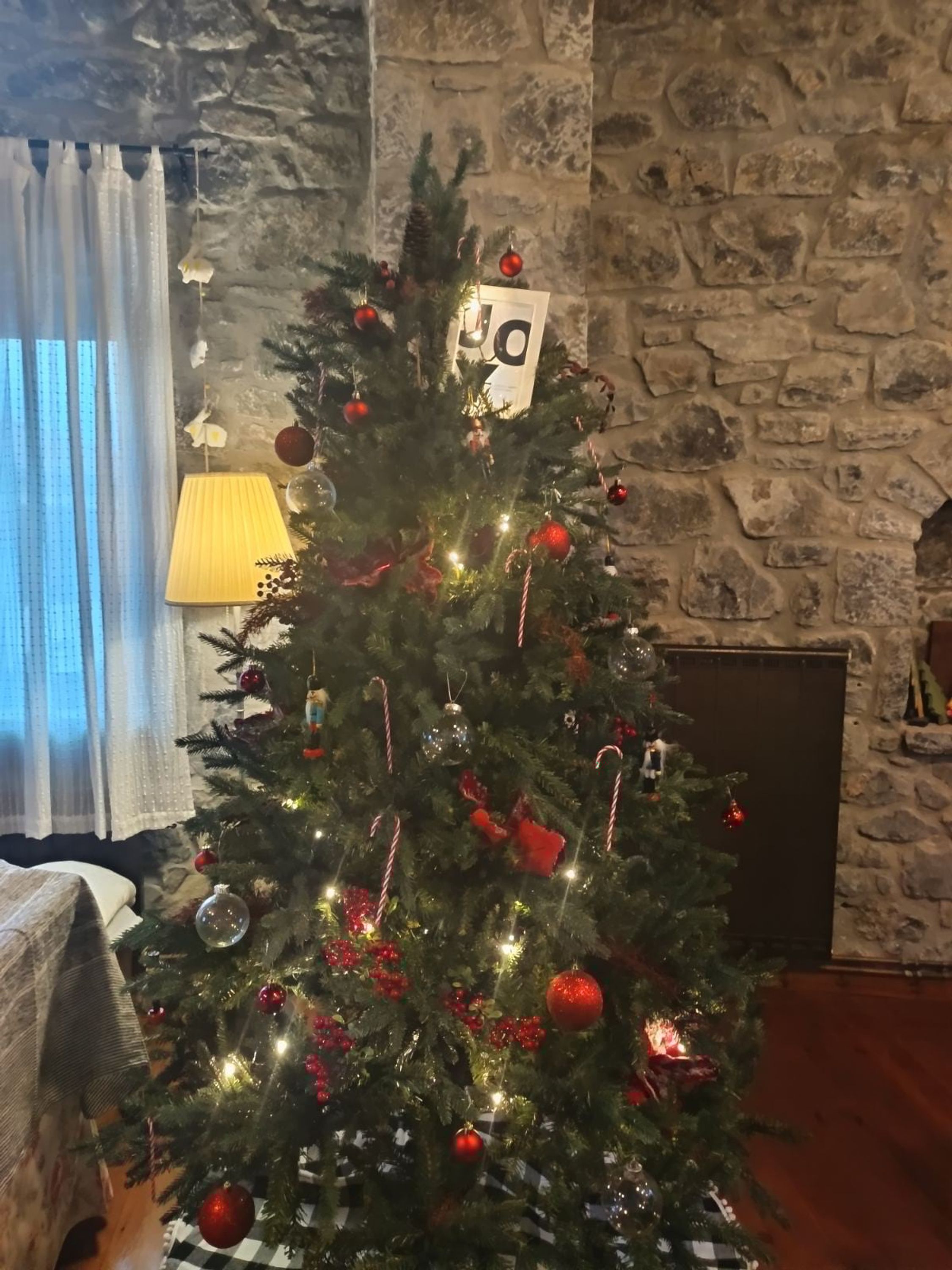 A decorated Christmas tree in a room with stone walls, a lamp, and a checkered floor.