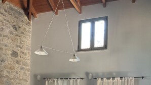 A dining area with a wooden table and chairs, a stone wall, and a window with curtains. - Vitina Number 5 House (Gortynia)