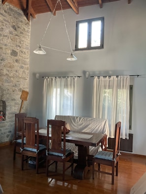 Un coin repas avec une table et des chaises en bois, un mur en pierre et une fenêtre avec des rideaux.