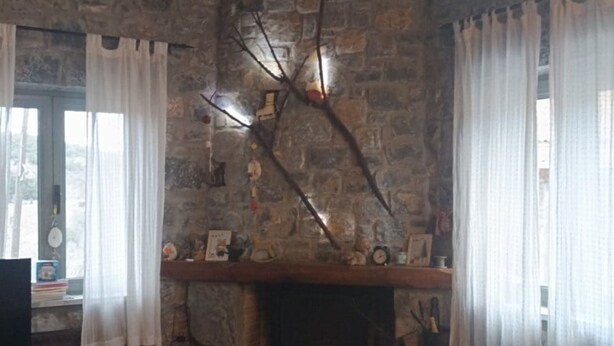 A rustic stone-walled room with a fireplace, wooden furniture, and a hanging light fixture. - Vitina Number 5 House (Gortynia)