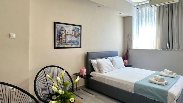 A modern bedroom with a bed, a desk, chairs, a potted plant, and a painting on the wall. - Monastiraki 103 Superhost Hub (Athens)