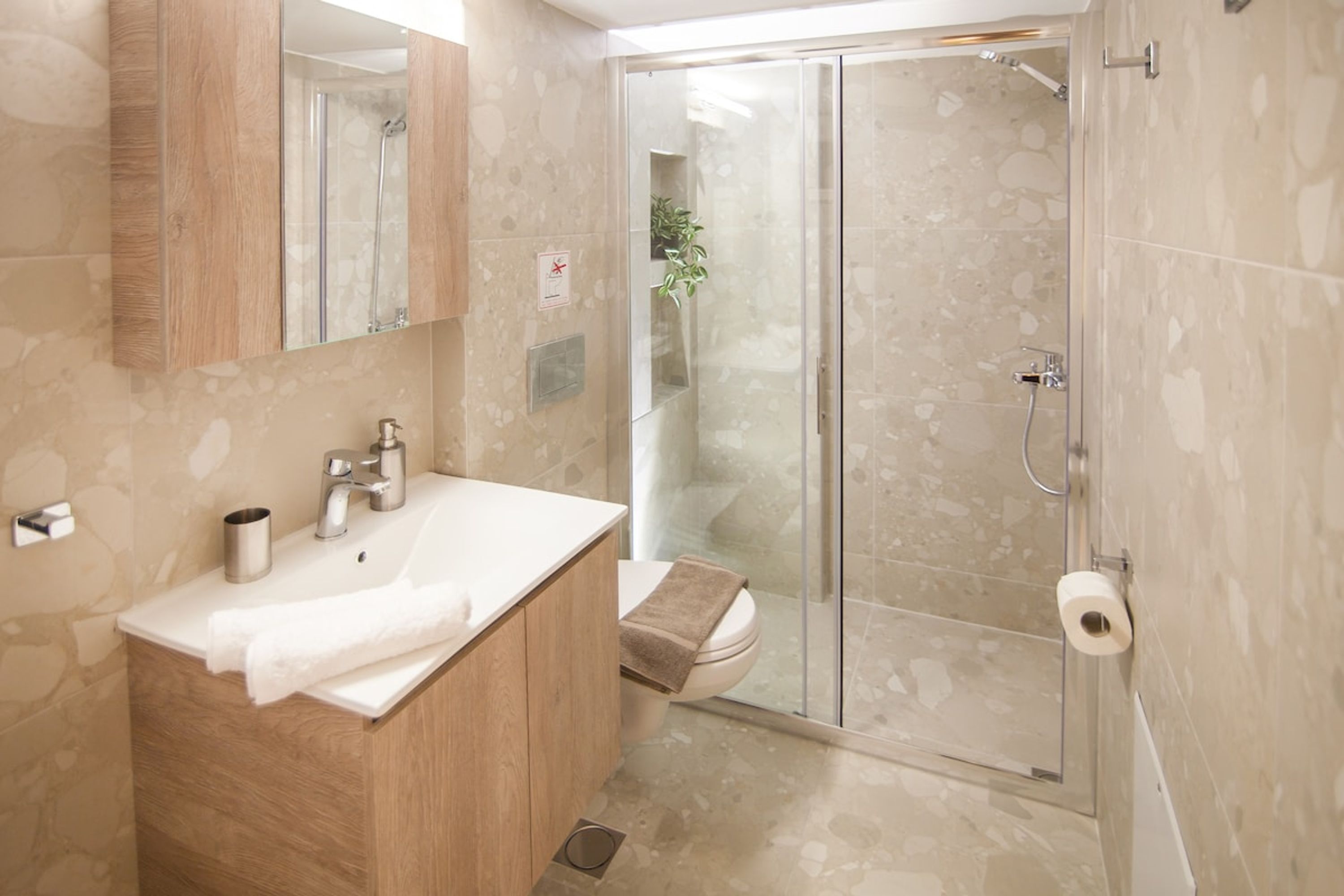 A modern bathroom with a wooden vanity, a glass shower enclosure, and a toilet.