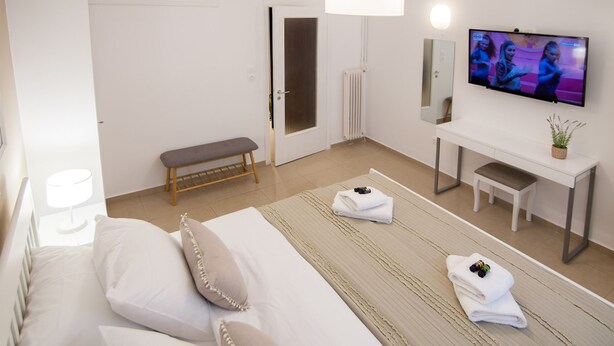 A hotel room with a bed, a bench, a desk, a TV, and a radiator. - The Acropolis Erenest (Athens)