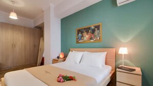 A hotel room with a bed, a nightstand, a lamp, a painting on the wall, and a wooden wardrobe.