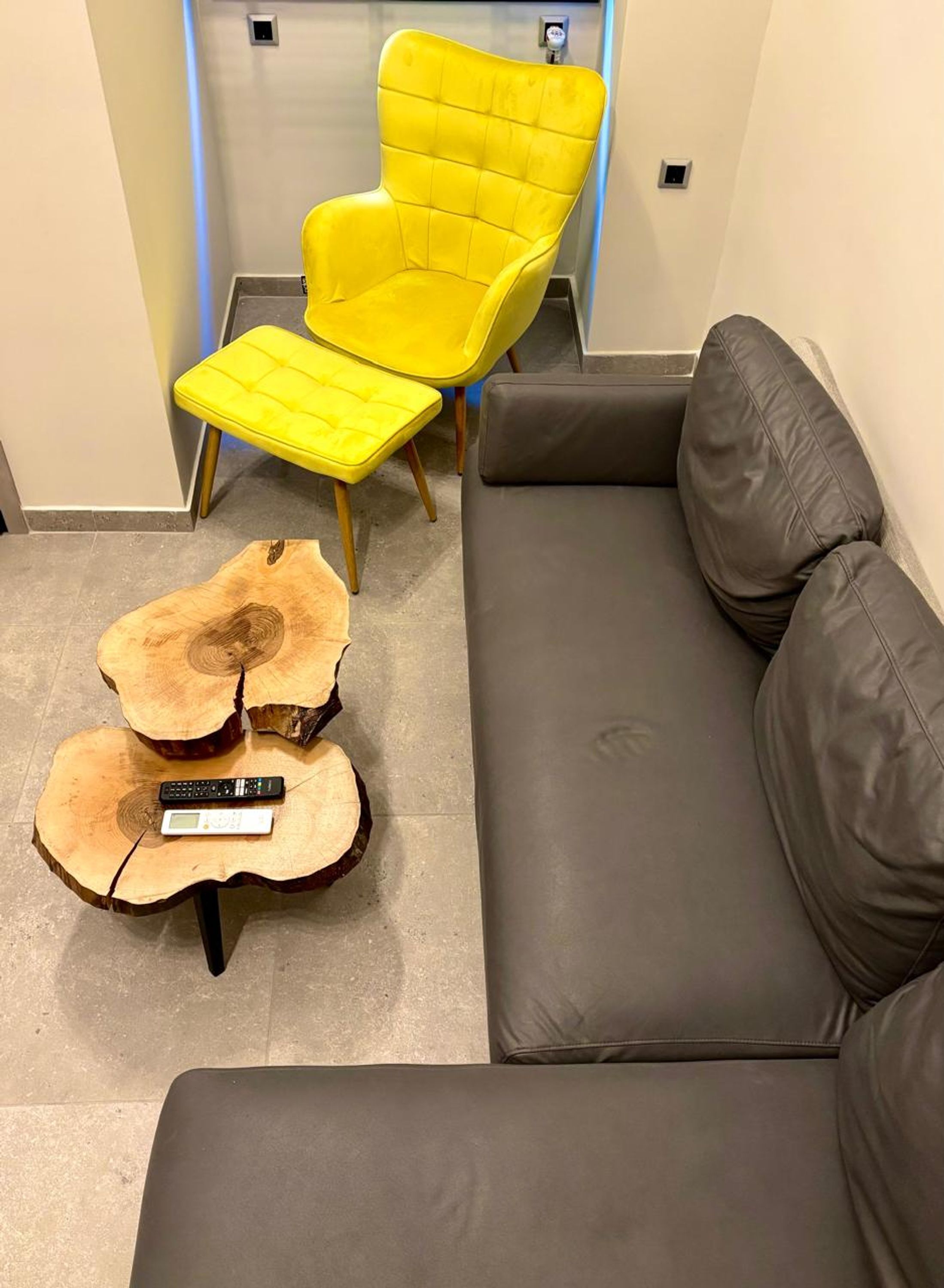 Ein modernes Wohnzimmer mit einem grauen Sofa, einem gelben Sessel und einem Couchtisch aus Baumstämmen.