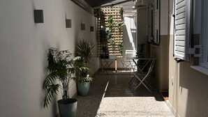A narrow corridor with potted plants, a wooden lattice wall, and a table with chairs.