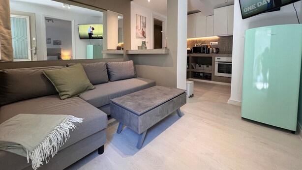 A modern living room with a grey sofa, a small ottoman, and a television mounted on the wall.