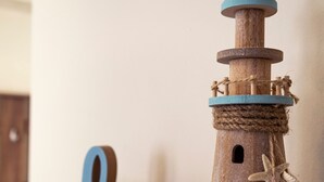 Un modellino di faro in legno con dettagli in corda e una decorazione a stella marina su uno scaffale.