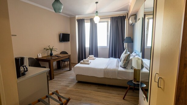 Una camera d'albergo con un letto, una scrivania con la macchina del caffè, una sedia, una lampada e uno specchio.