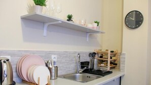 Una cucina con un piano di lavoro bianco, un lavello in acciaio inossidabile e una sveglia appesa al muro.