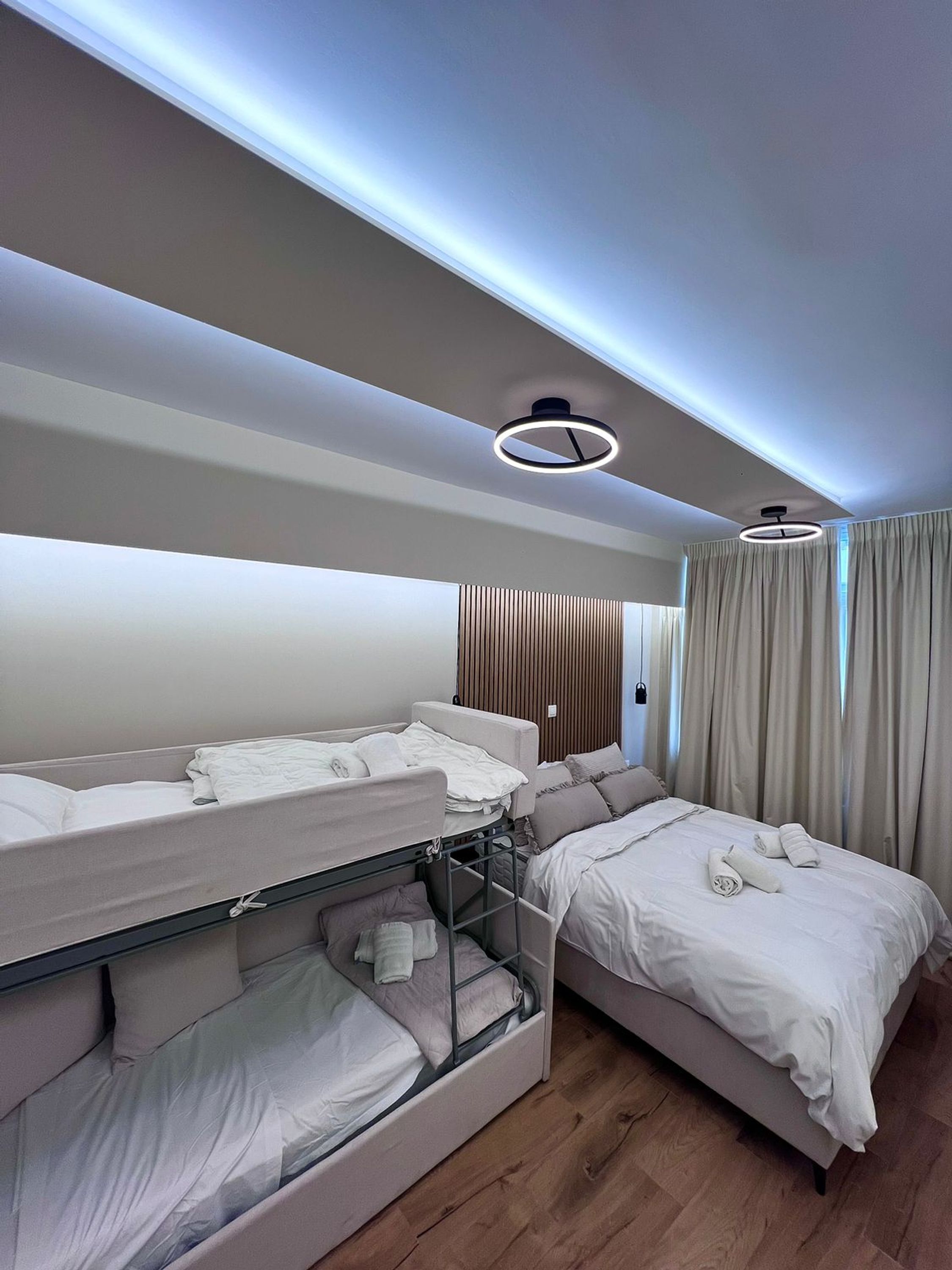 Een hotelkamer met stapelbedden, een houten vloer en een moderne plafondlamp.