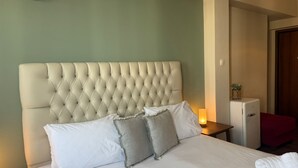 Habitació d'hotel amb un capçal de llit amb guarnició, un llit amb almoines blanques i grises, una tauleta de nit amb una làmpada i una cadira vermella.