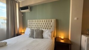 Habitació d'hotel amb un llit gran, un panell de capçal tapissat, dues làmpades laterals i un aparell d'aire condicionat fixat a la paret.