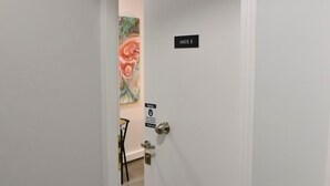 A door labeled "IANOS B" with a notice sign, a chair, and a partial view of a room with a colorful painting. - Athens Ianos B by Super Host Hub (Athens)