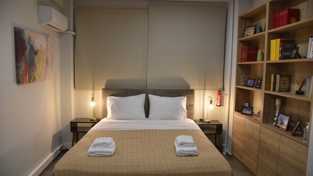 A hotel room with a bed, bedside tables, a bookshelf, and a painting on the wall. - Athens Ianos B by Super Host Hub (Athens)